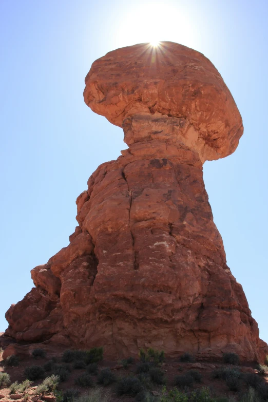 a big rock formation with a sun glaring in the distance