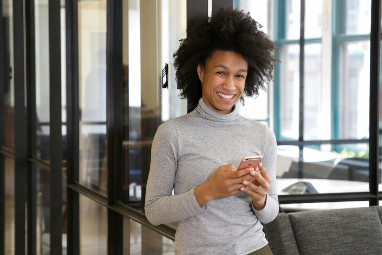 a woman smiling in a gray turtle neck top, holding a phone