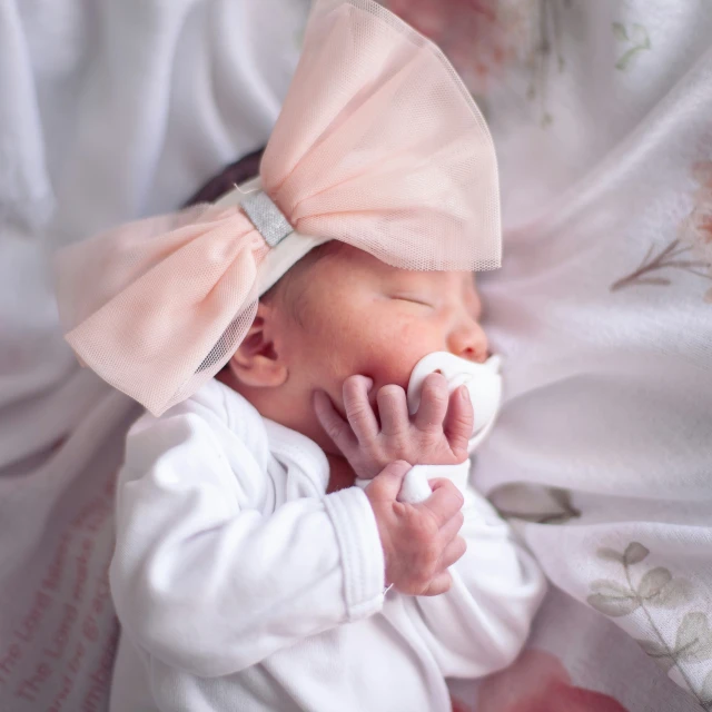 a baby sleeping with a pink bow on its head and a white cup