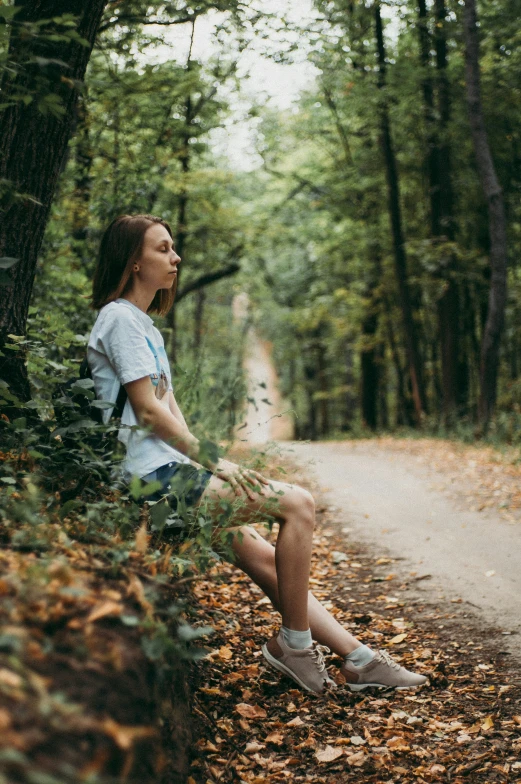 a woman sits on the ground outside in the woods