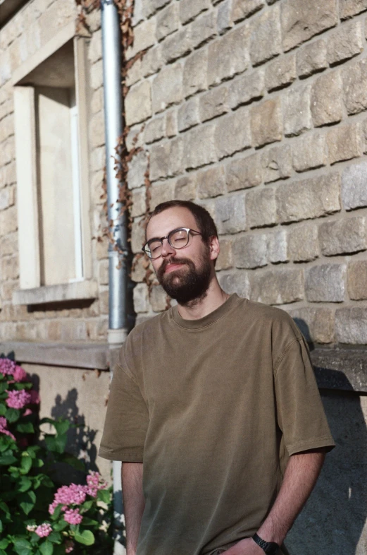 a bearded man in glasses stands in front of a building