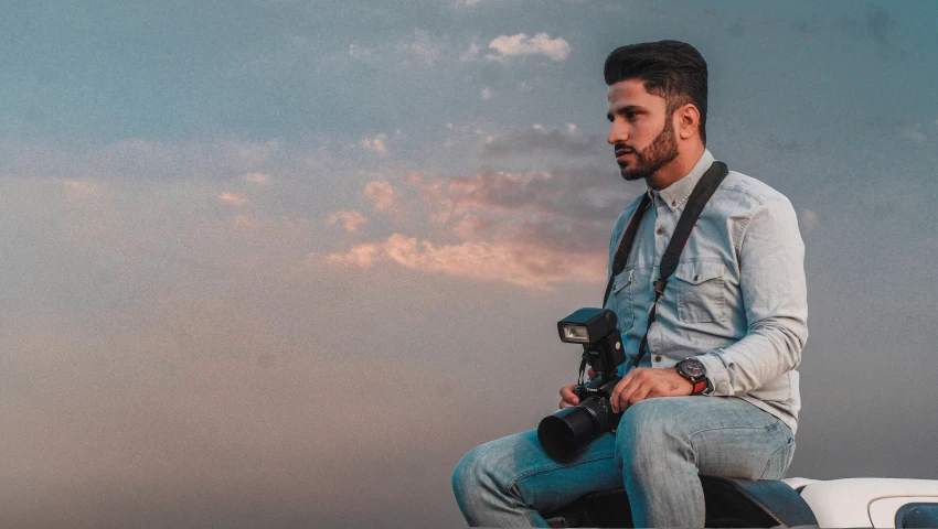 a man holding a camera sitting on the hood of a car