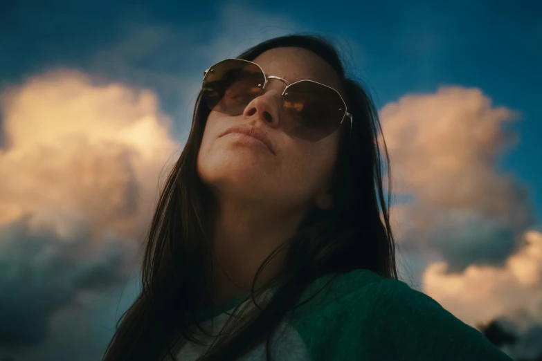 a woman wearing glasses standing in front of clouds