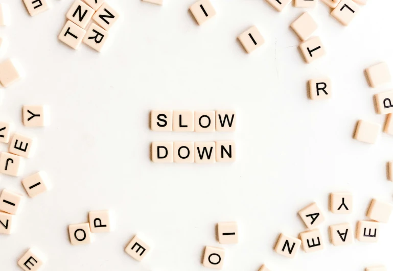 scrabbled letters spelling slow down are arranged by letters in the shape of letters