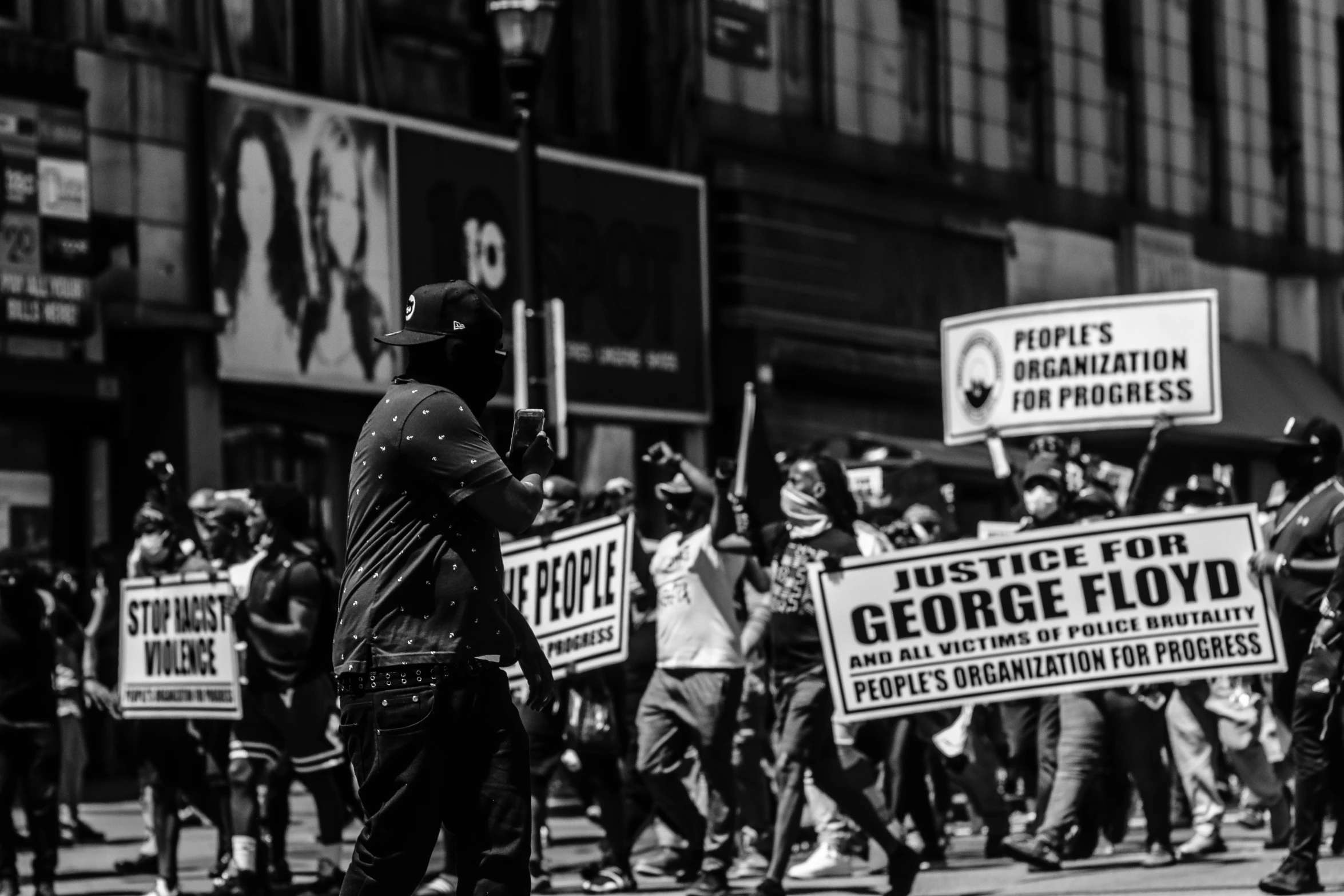 protesters with police helmets hold up signs as they walk down a street