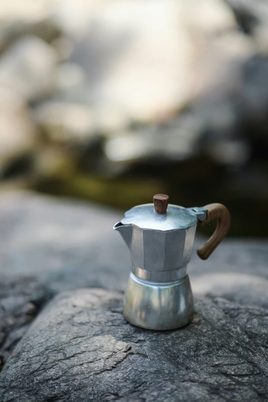 a small, glass and metal pot with handle sitting on a stone