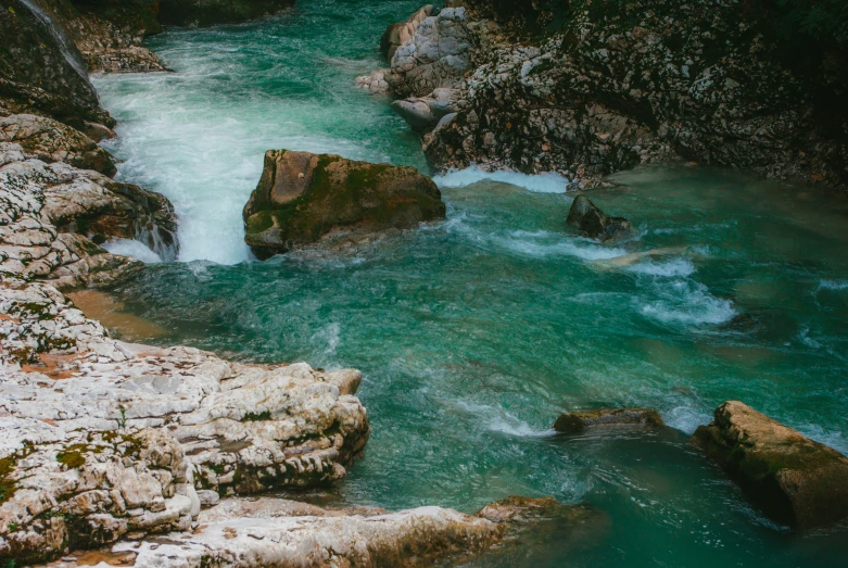 a river surrounded by rocks and moss with green water