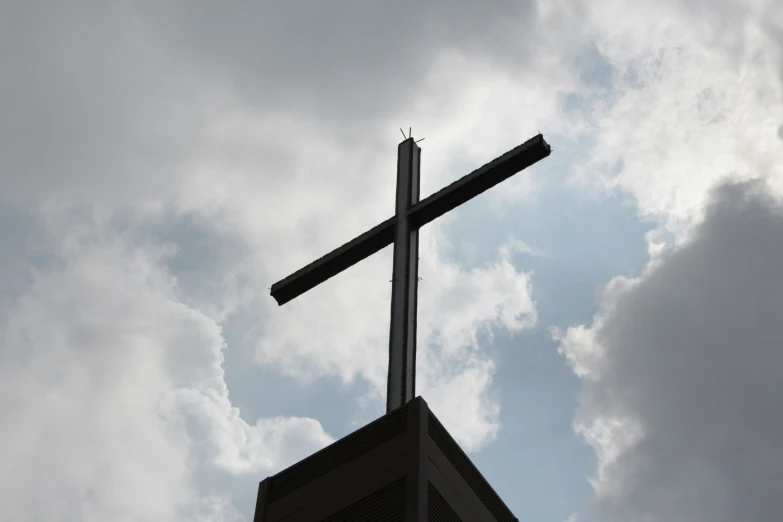 cross sitting on top of a church with clouds in the background