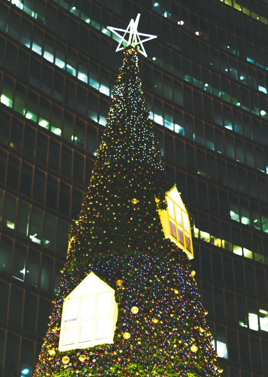 an illuminated christmas tree stands on the street at night