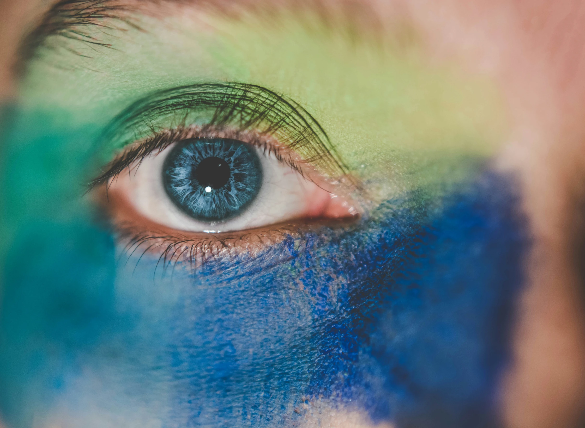 the eyes and body of a person with bright painted blue and green makeup