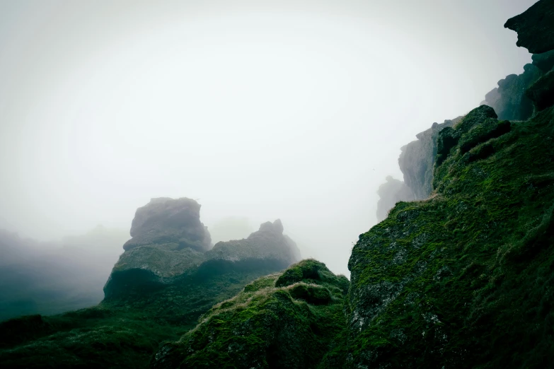 misty landscape with large rocks and grass growing up the side