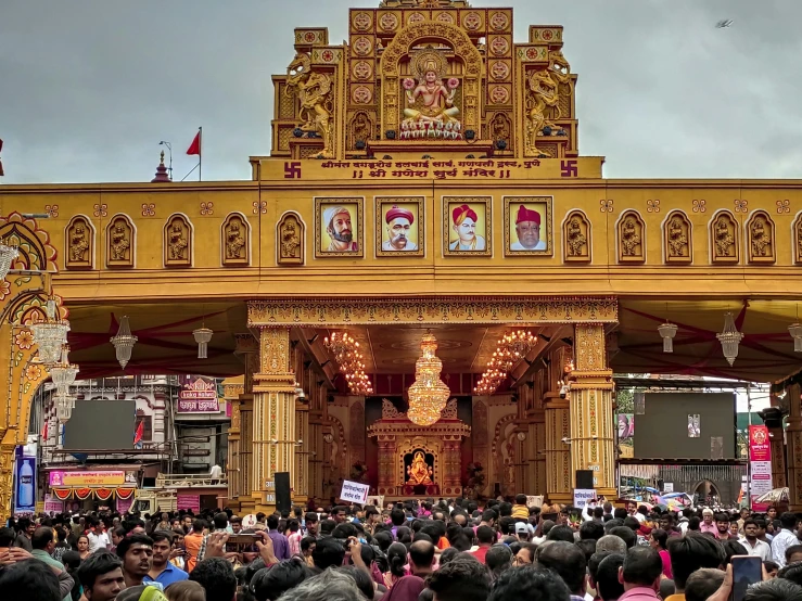 an ornate shrine on a crowded street is decorated with gold and red, but the shrine has two pillars at the end