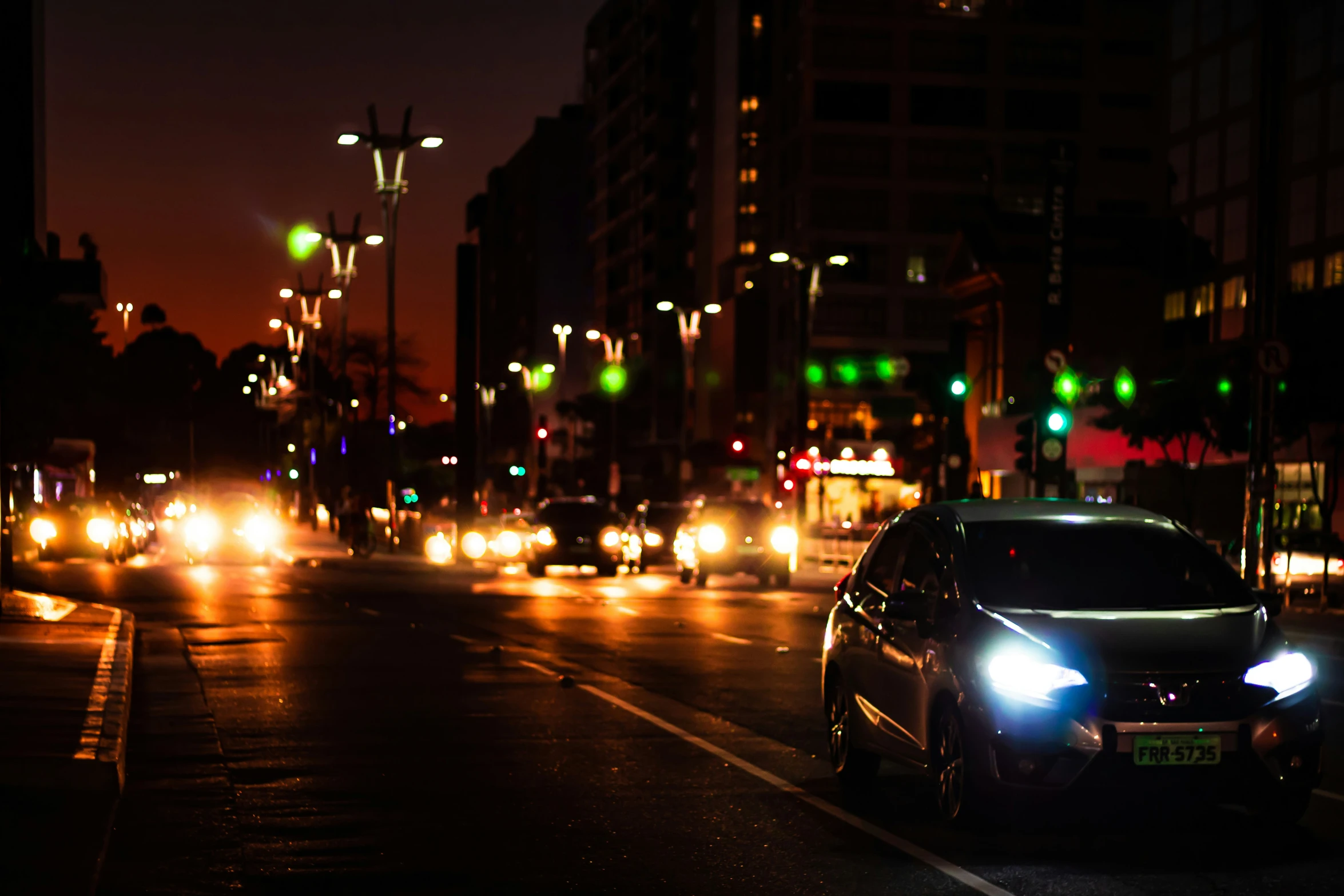 a car with its headlights turned on driving down a busy city street