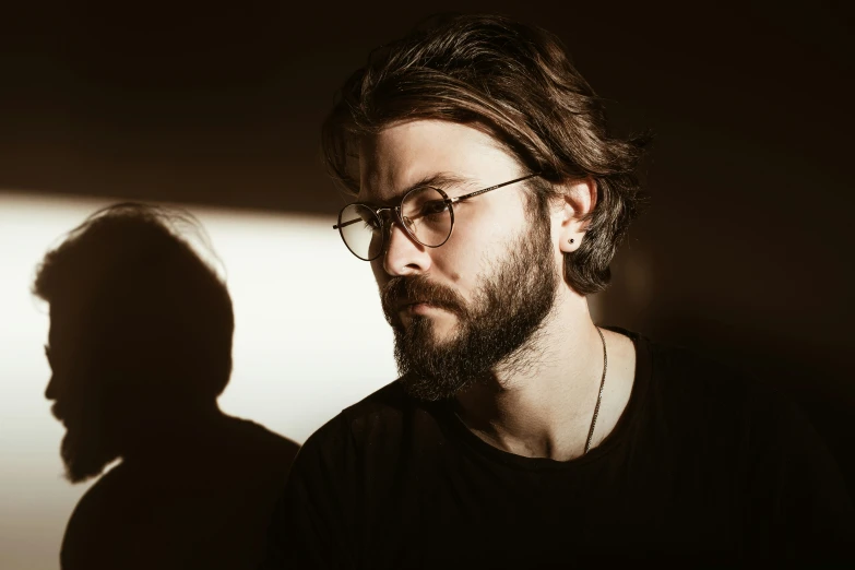 a man with glasses and beard standing next to a wall