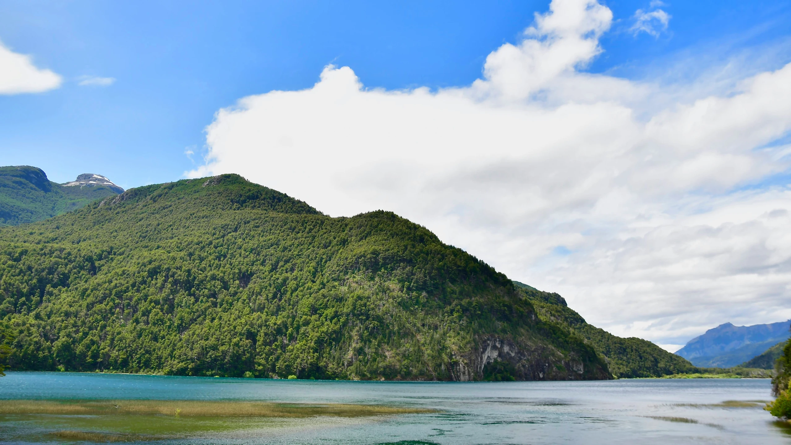 a lake surrounded by mountains and trees under a cloudy blue sky