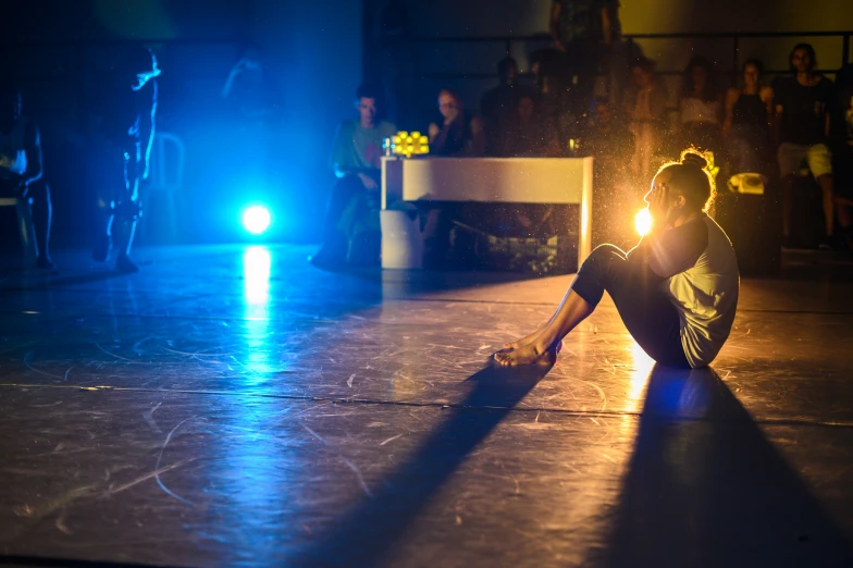 woman crouched in the corner, on the floor illuminated by brightly colored light