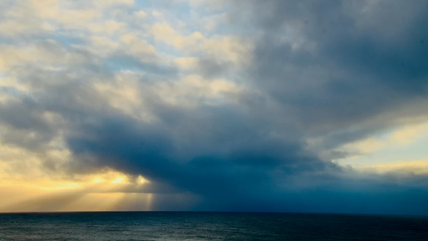 a very dark sky over the ocean with sun rays