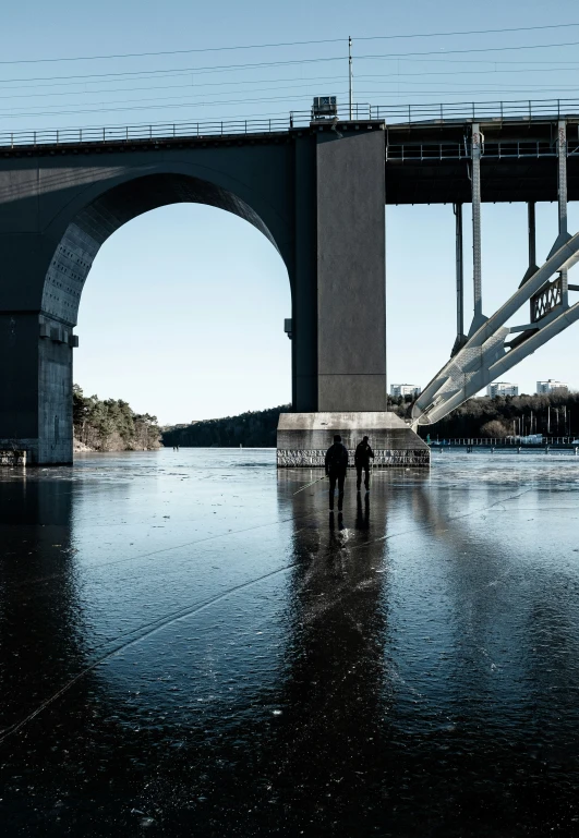 a couple walking down the beach below a bridge