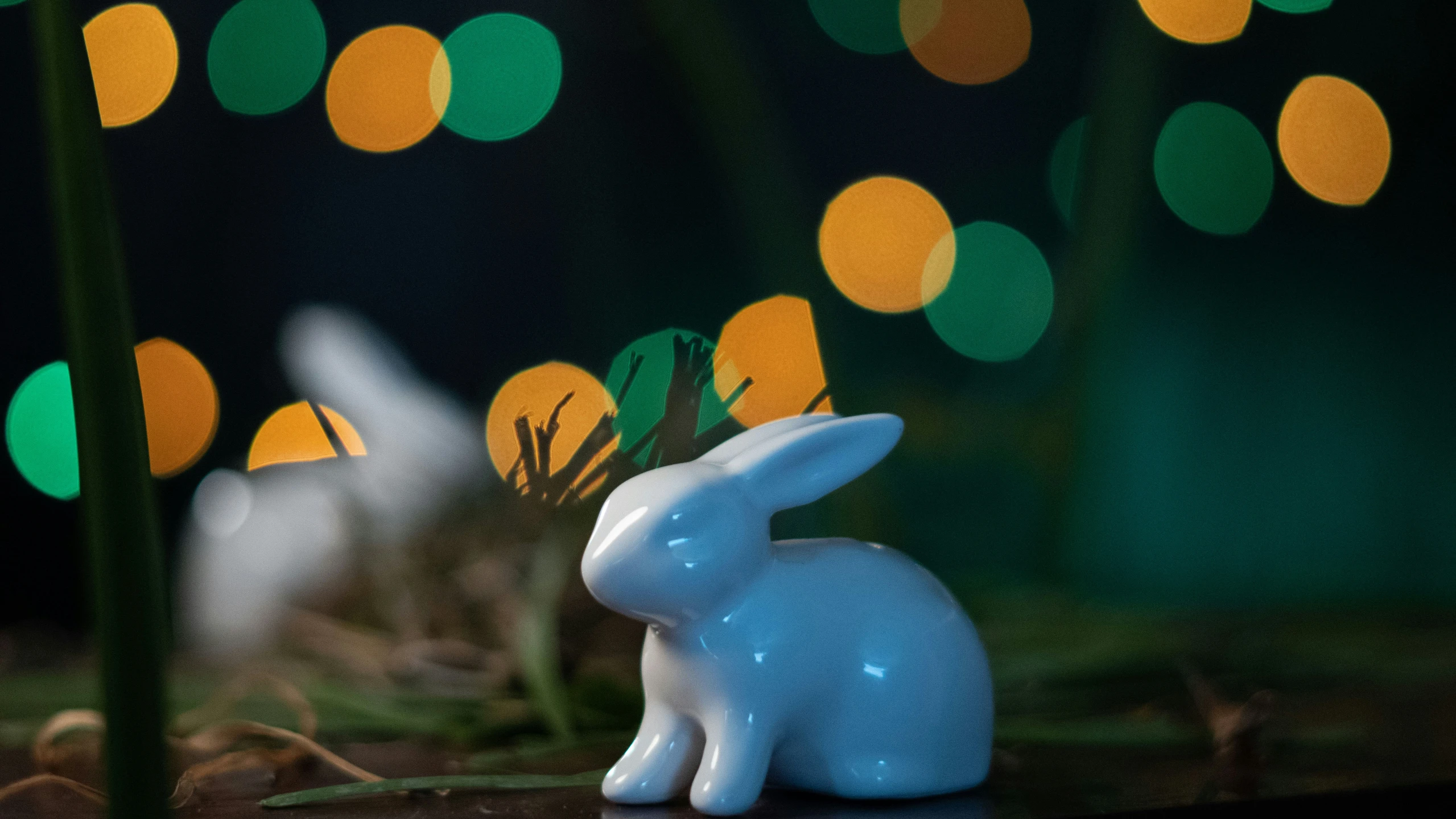 two small ceramic bunnies are in front of blurred lights