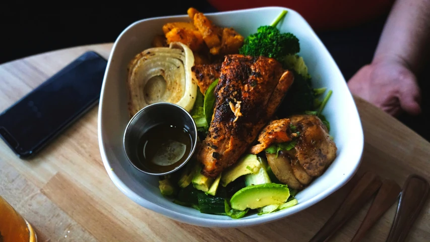 a bowl of food sitting on a table with a phone beside it