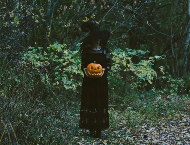 a woman in a black dress holding an orange pumpkin