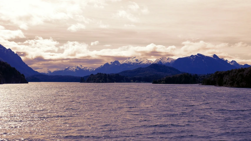 a body of water surrounded by trees with snow covered mountains