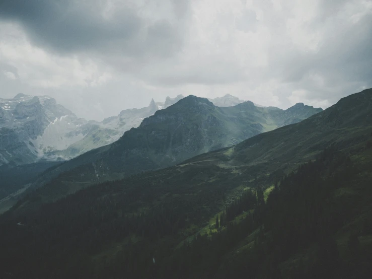 a mountain range under storm clouds with green grass on the bottom