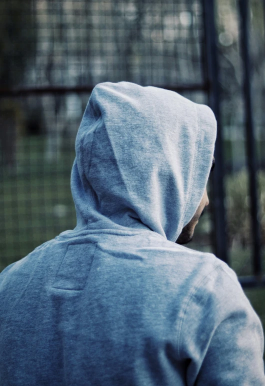 person in gray hoodie staring at a bird cage