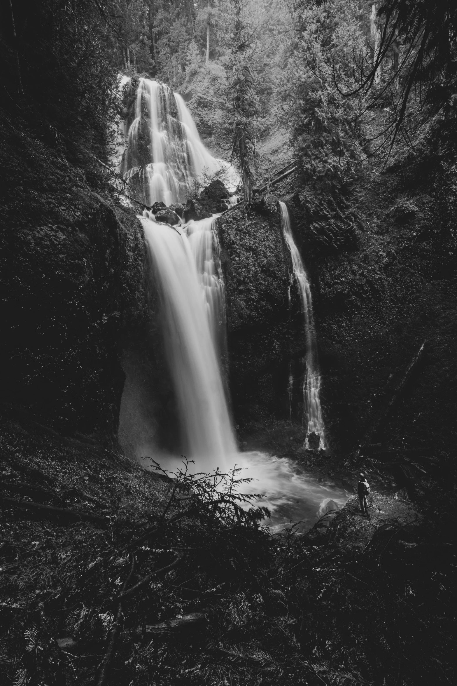 a black and white image of a man in front of a waterfall