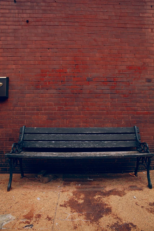 an old, black wooden bench near a brick wall
