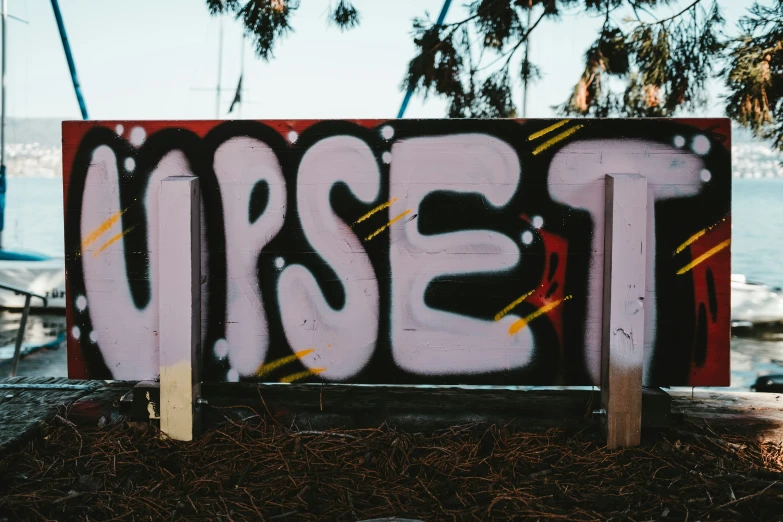 a wooden sign with black, yellow and red graffiti written on it