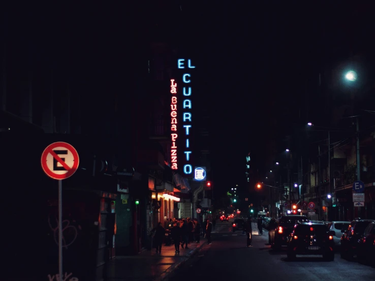 a neon sign sits above a night - time city street