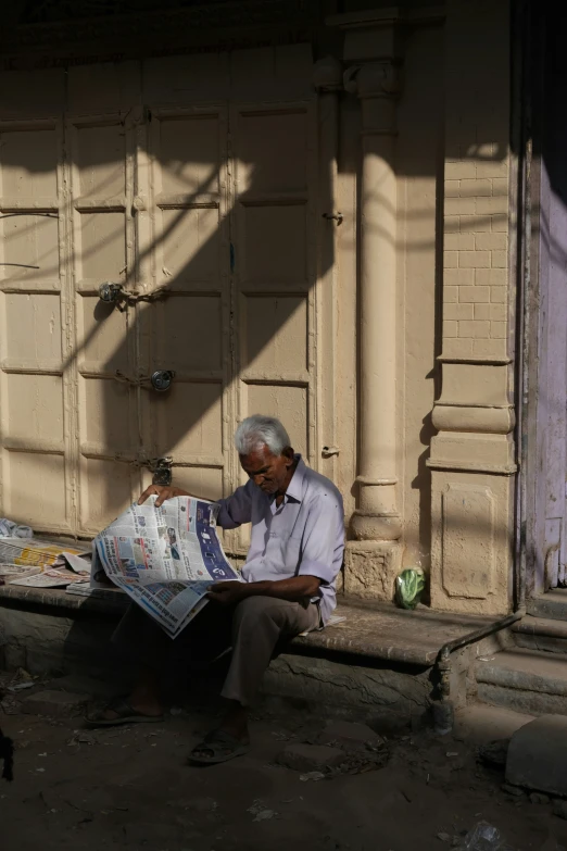 a man sitting on a stone bench reading a newspaper