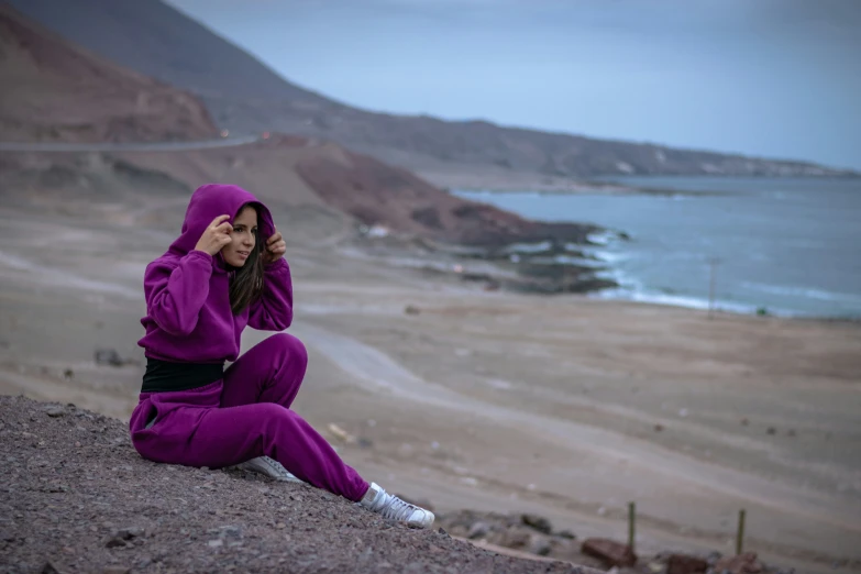 a woman in purple sits on a rock near the ocean