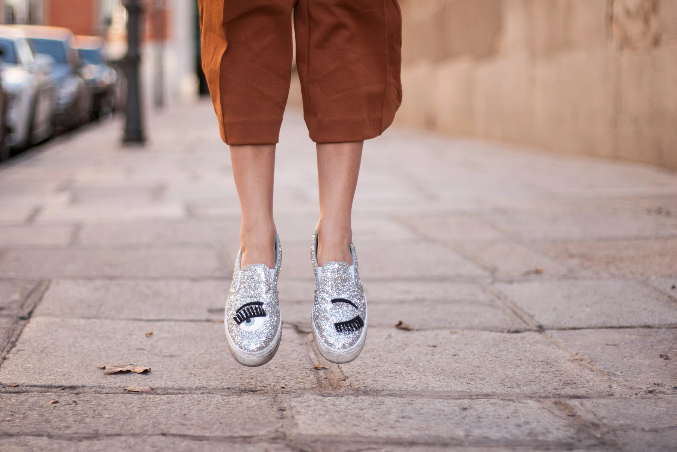 someone wearing silver slippers walks down the sidewalk