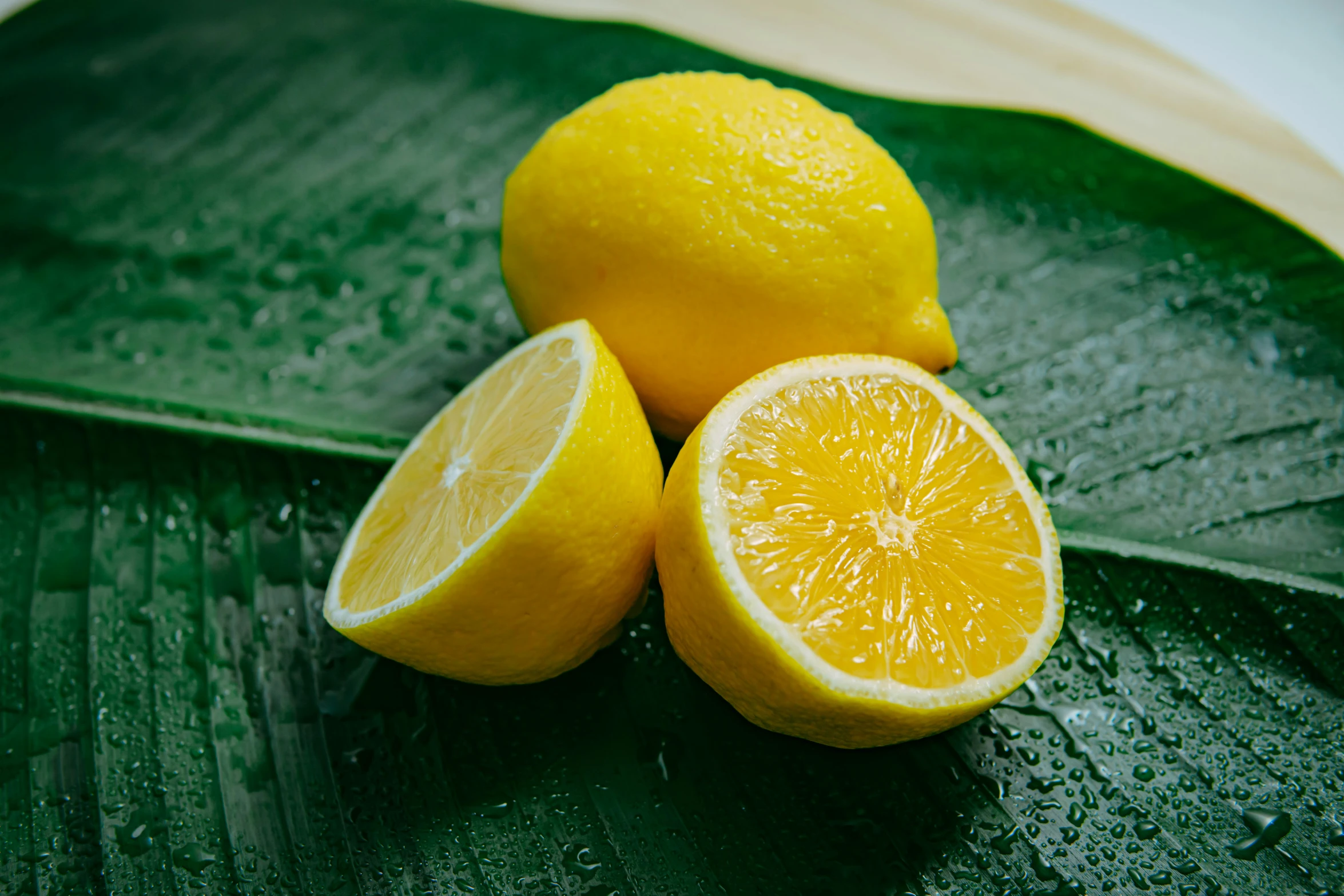 two lemons, one cut in half, are sitting on a large leaf