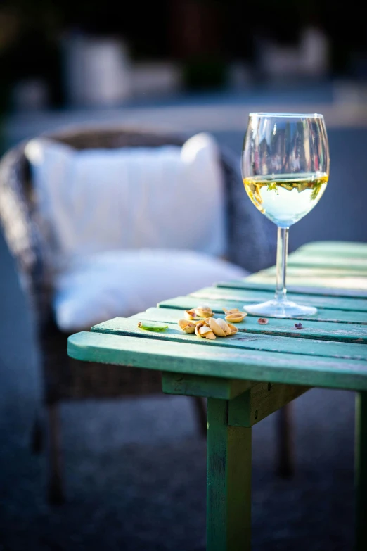 a glass of white wine sitting on top of a green table