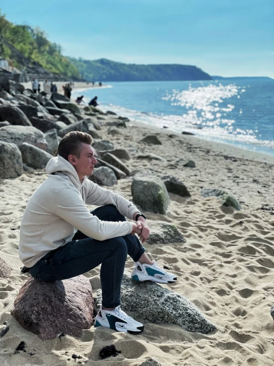 man sitting on large rock at sandy beach