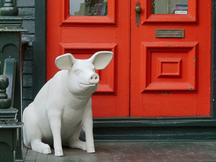 a statue of a pig sitting on the ground in front of a red door