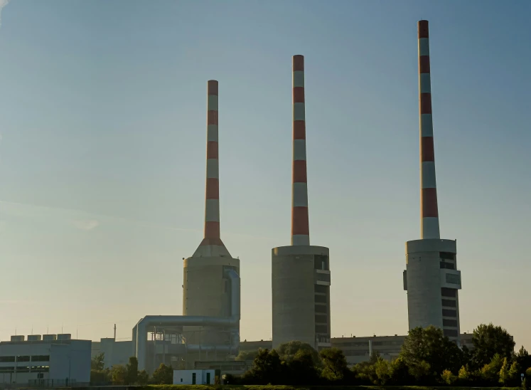 two smoke stacks rise over a river, and a building with four chimneys