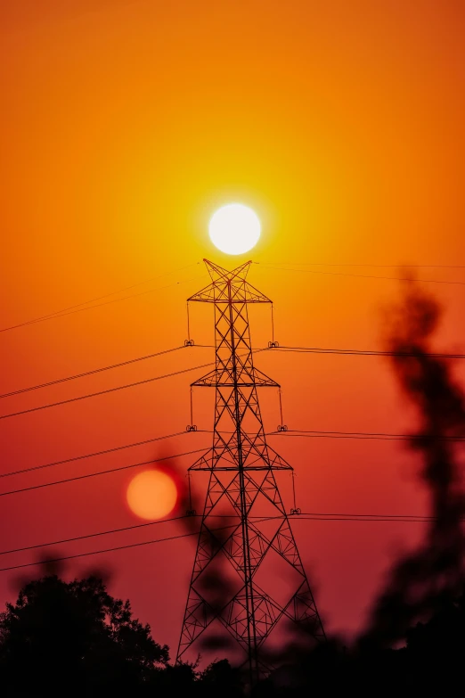 an electric tower with the sun in the distance