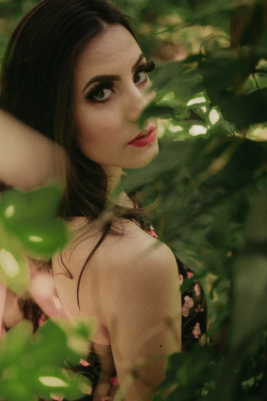 a woman with dark hair is hiding in the leaves of trees