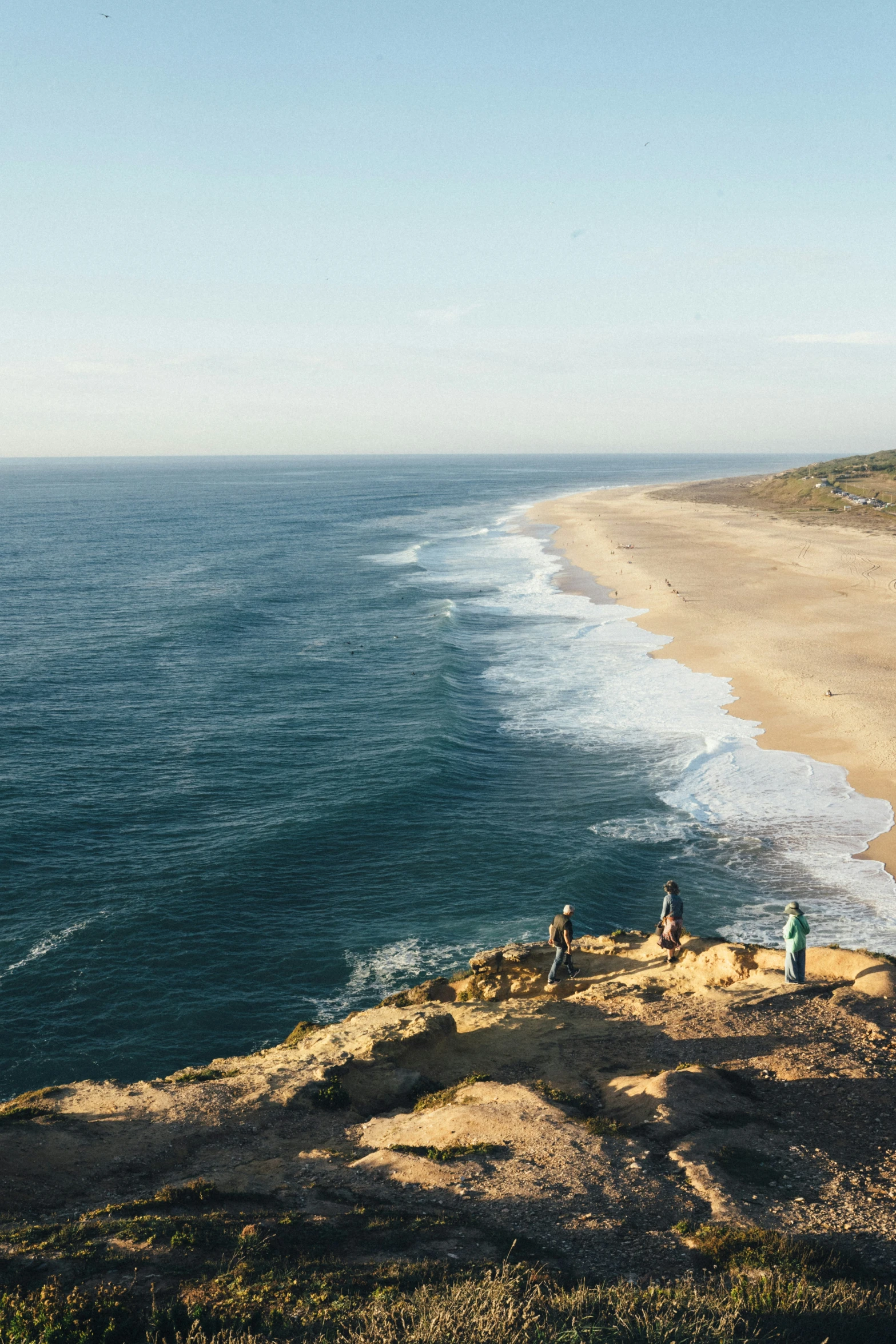 three people stand on the edge of a cliff overlooking a beach