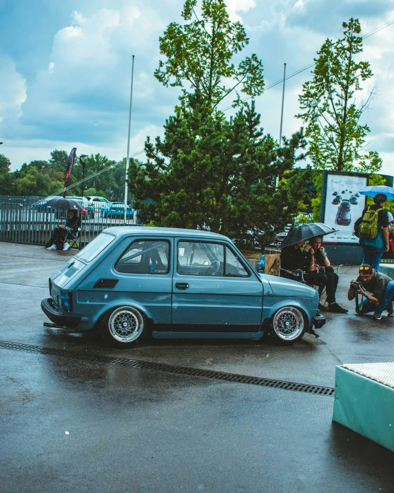 people getting ready to board an old car while a man kneels in the street