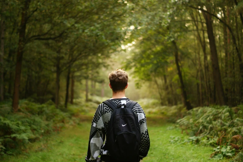 there is a young man with a backpack on the side of a forest trail