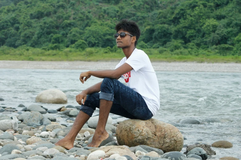 a man is sitting on a rock near a river