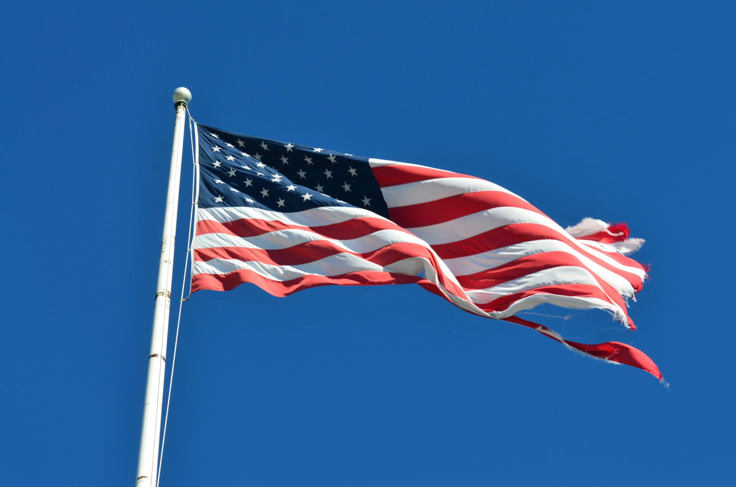 the american flag blowing in the wind under a bright blue sky