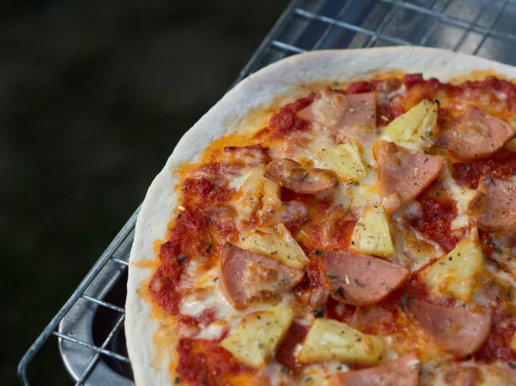 a sausage and pineapple pizza sitting on a grill