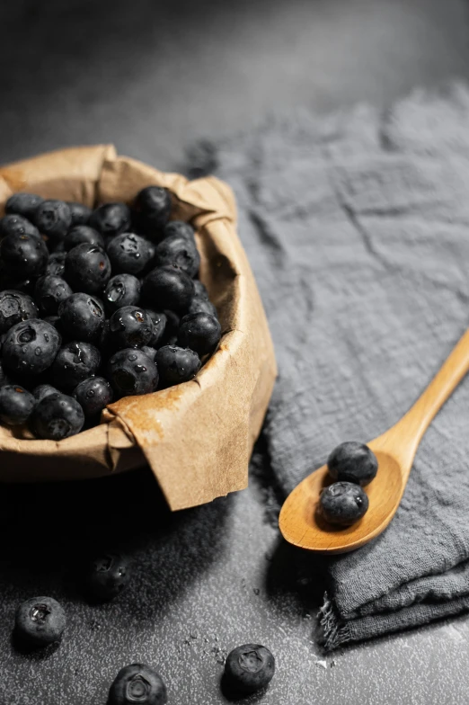 a brown paper bowl filled with blueberries next to a wooden spoon