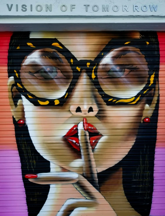 a lady holding a cigarette and wearing glasses while standing in front of a wall painting